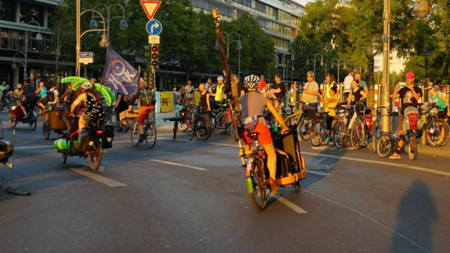Diverse Lastenradfahrende und adfahrende mit Anhänger umkreisen die Mittelinsel auf der Kantstrasse gegenüber des Bikini Berlin auf der September Demo.
DIe Lastenradfahrenden vom ersten Bild bewegen sich nun von der Kamera weg.