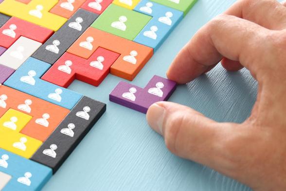 Colourful tangram puzzle blocks with people icons on a pale blue wooden table. Image by tomertu via Shutterstock.