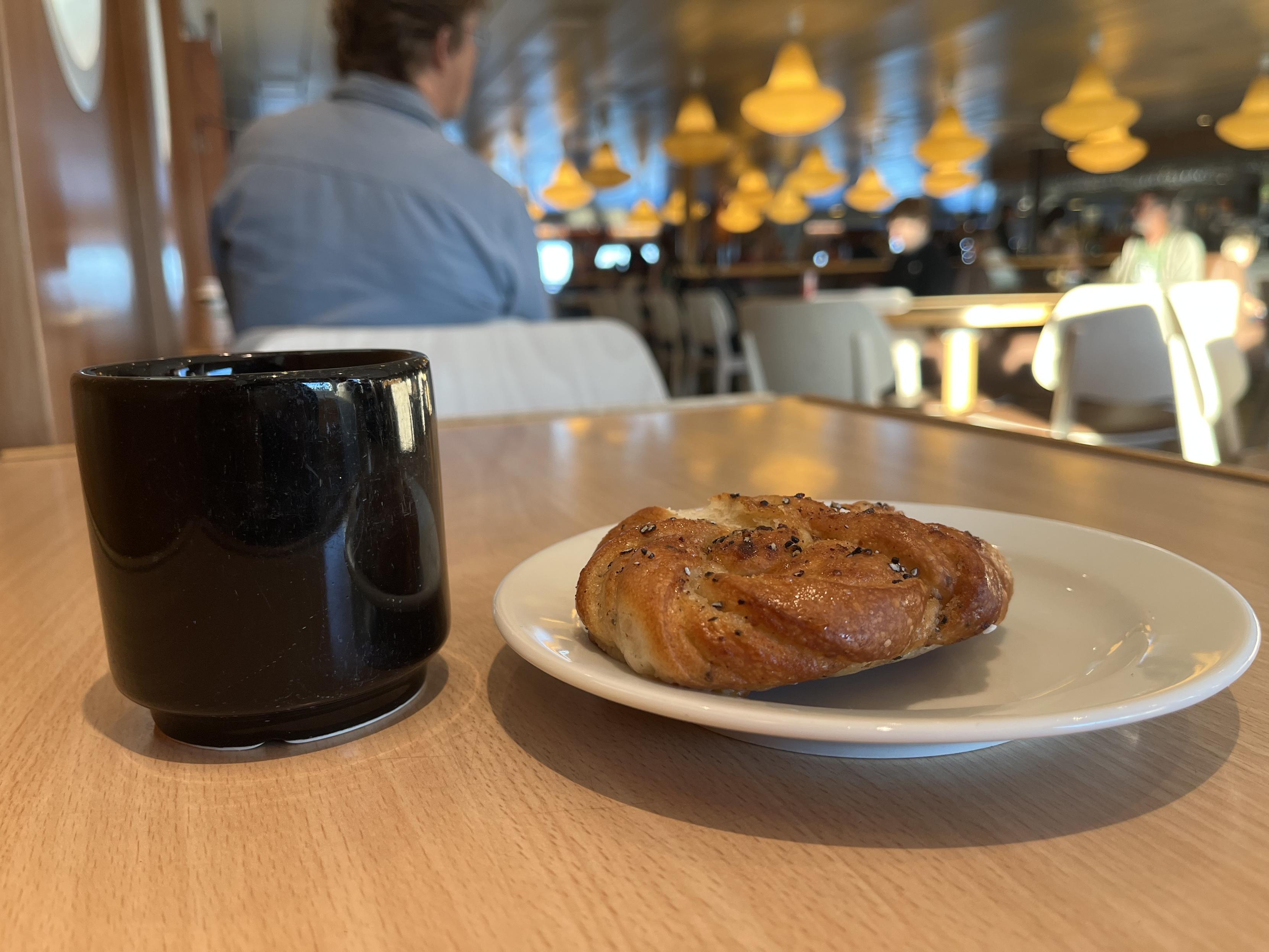 Mug of coffee and a plate with a cardamom roll, like a cinnamon roll but with cardamom, on a table in the cafeteria of a ferry boat on its way from Åland to Sweden