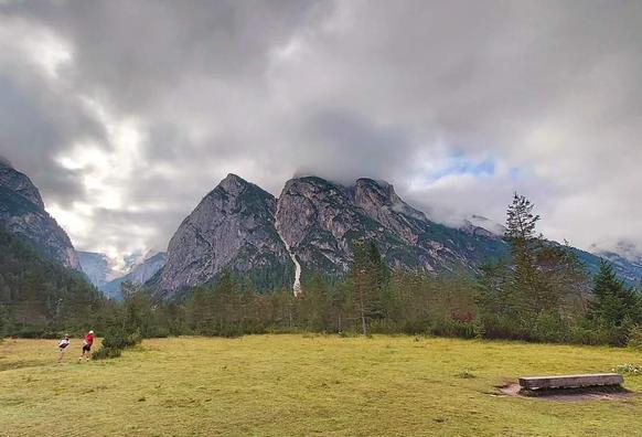 Drei Bergspitzen, davor eine Alpwiese. Über den Berge dicke dunkle Wolken. 