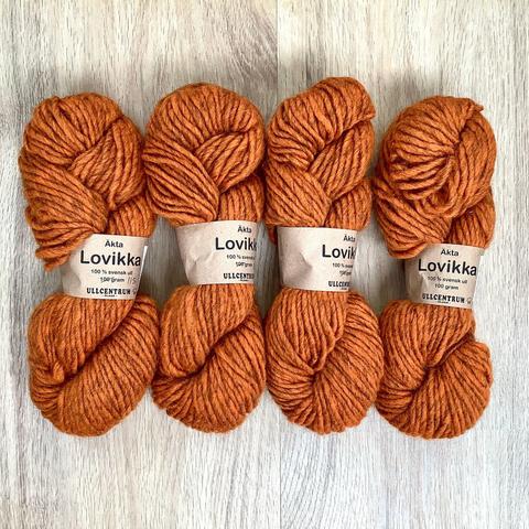 4 skeins of orange bulky weight yarn on a light wooden background.