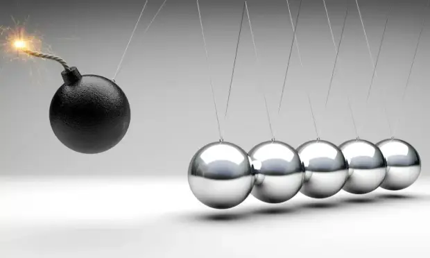 A lit bomb swinging towards a row of silver balls, all on strings.