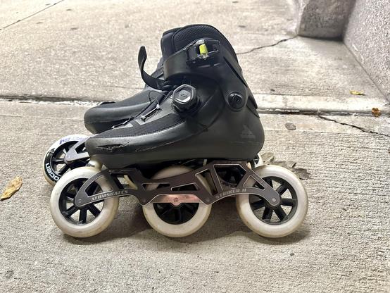 Photo of a pair of inline skates on the sidewalk. The are Rollerblade Revv BOA boots mounted on Striker II frames (3x110), with Inline Warehouse branded RB Hydrogen wheels. Yes, there is a hard scrape along the side of the tow end of the near boot due to one or another fall.