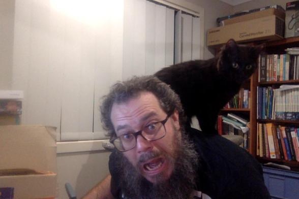 Photo of author in some pain and distress but laughing about it. 

They are leaning forward with a black parrot/kitteh perched on neck and shoulder, digging their claws in 😜