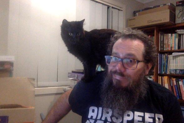 Photo of author in some pain and distress but laughing about it. 

They are leaning forward with a black parrot/kitteh perched on neck and shoulder, digging their claws in 😜