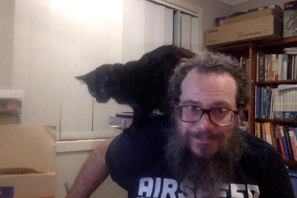 Photo of author in some pain and distress but laughing about it. 

They are leaning forward with a black parrot/kitteh perched on neck and shoulder, digging their claws in 😜