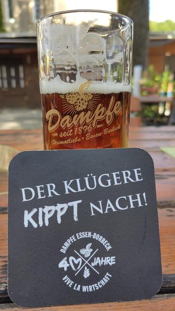 Bierglas gefüllt mit bernsteinfarbenem Salonbier. Biedeckel mit der Aufschrift: Der klügere kippt nach. 40 Jahre Dämpfe in Essen. Vive la Wirtschaft