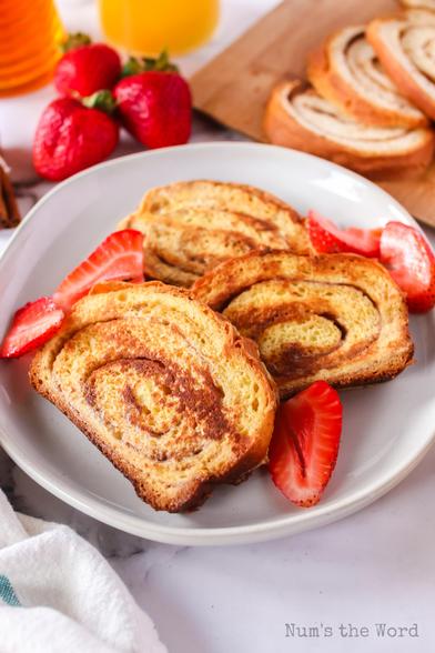 3 slices of cinnamon swirl french toast on plate with sliced strawberries around it. 