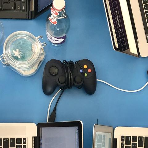 A gamepad on a table in a cafe surrounded by laptops