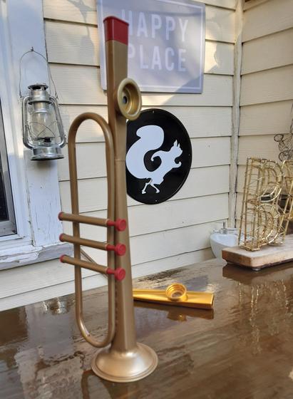 A kazoo shaped like a trumpet. It's gold coloured and about eleven inches long with three red keys, over three moving values, and has a red mouth piece.  It is pictured on a shiny wood bar top. 