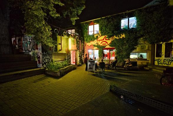 an exterior shot of the next event location. people sit outside in front of an illuminated window.