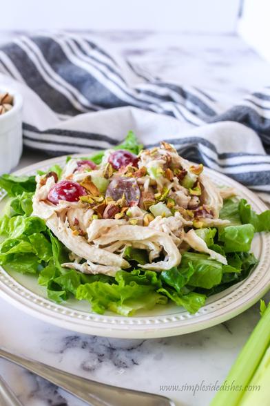 Side view of a bed of lettuce with chicken salad on top.  Then sprinkled with chopped pistachios.