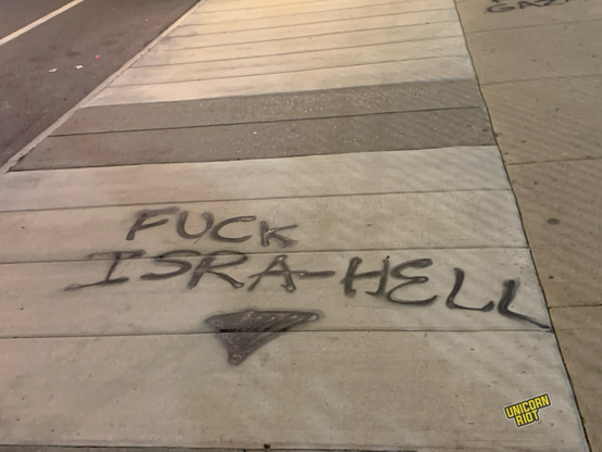 “Fuck Isra-Hell” spray painted in black above a black upside down triangle on a wide sidewalk