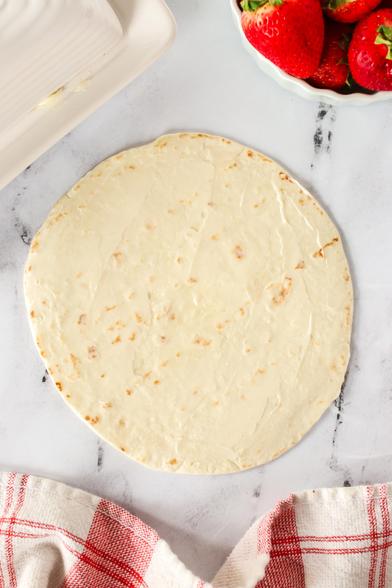 A single tortilla laid out on counter with butter smeared all over it. 