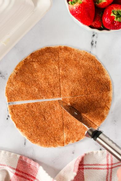 Cinnamon sugar on a tortilla chip with a pizza cutter cutting it into chips. 