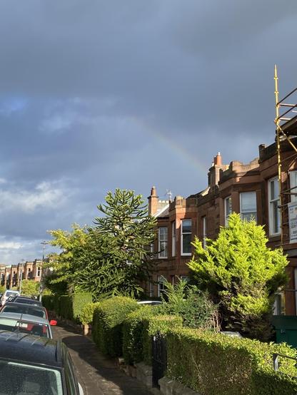 Faint rainbow edge in a moody sky behind a row of terraced houses, sun illuminating the foreground 