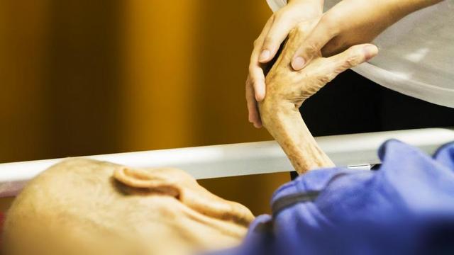 Elderly person in hospital bed holding hands with someone.