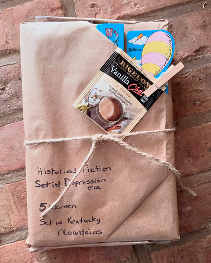 book wrapped in brown paper with a straw tie around it. a little pocket has an eraser and a bookmark. a clothing pin holds a vanilla chai tea bag. 