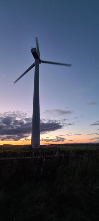 A wind turbine almost silhouetted against the sky, which is deep into sunset. There is only a small orange glow left along the horizon.