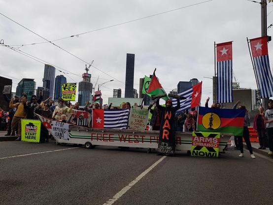 Free West Papua boat on wheels with west Papua and Kanaky flags in the street with high rise building skyline behind 