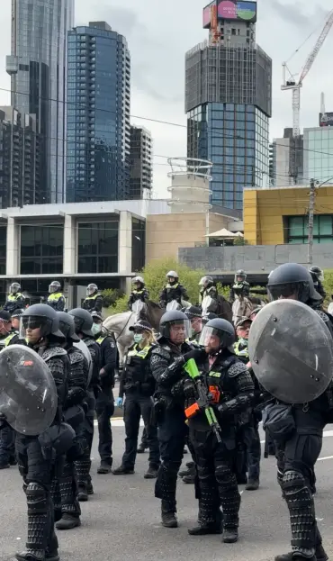 Skyline of tall city business district buildings 
Police on horseback 
Police with riot shields, body armour, helmets and visors and batons One carries a rubber bullet firing weapon.