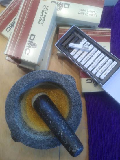 Bild eines Mörsers mit Schellack, noch sehr grob gemörsert, Pastellkreiden, Stickgarnschachteln von DMC und violettem Woll-Stickgrund.
Bläue wird von Handstickern genutzt, um Stechpausen (Vorlagen) auf Stoff aufzuzeichnen. Im Hobbybereich wurde sie von Kopier- und Stoffstiften abgelöst, aber für Wolluntergründe und sehr große oder detailierte Motive ist die Methode nicht gut geeignet.
Ich muss mittlerweile meine Bläue selbst herstellen. Die ist dann zwar sehr grob gegenüber der Bläue, mit der ich gelernt habe, aber für meine Zwecke reicht es.