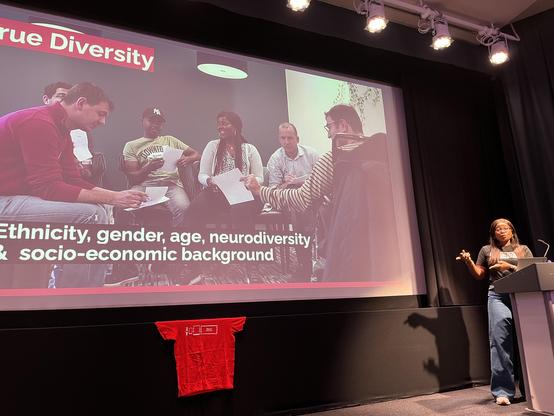 Gayle, a black woman in a Code Your Future tshirt, in front of a slide showing a collection of people and the caption True Diversity