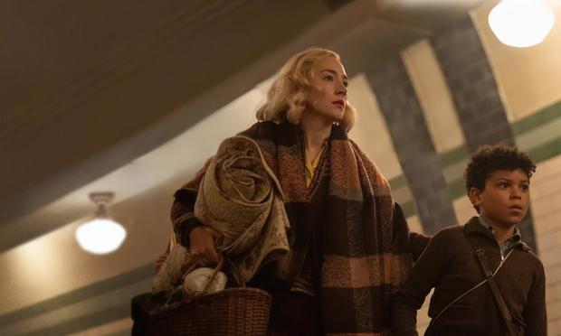 Scene from the 2024 film directed by Steve McQueen “Blitz”
A 1940s era hairstyle and dressed mother with blanket and bag, accompanied by young child; both are racing along into the Bethnal Green Undergound public transport Subway station .