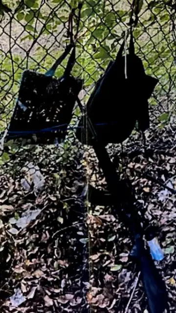 Two backpacks hanging on a chainlink fence with an Assault Riffle leaning against them.