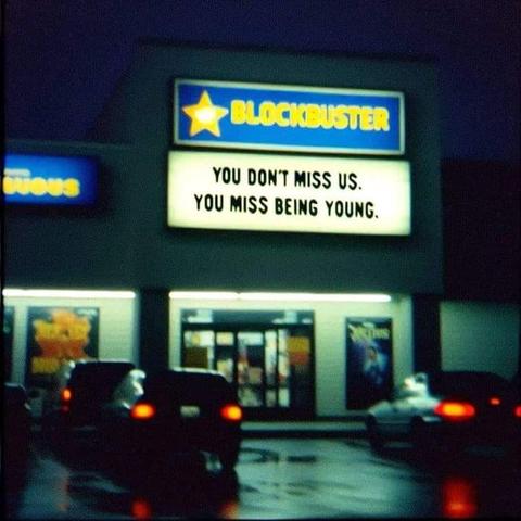 Night view of a Blockbuster video store from the parking lot. The marquee text reads "You don't miss us, you miss being young."