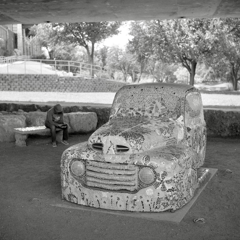 A black and white film photo. A vintage truck, covered in mosaic tiles, hangs out under a bridge in San Angelo, Texas. Sunday, September 1, 2024.
