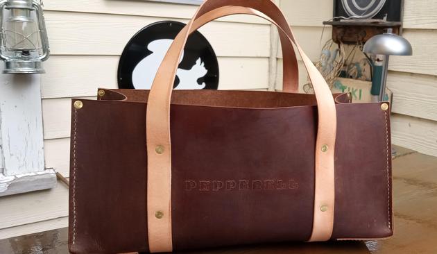 A dark tan leather utility tote with two light tan handles. "Pepperell" is embossed on both sides. The tote is 16 inches long and 8 inches tall. 