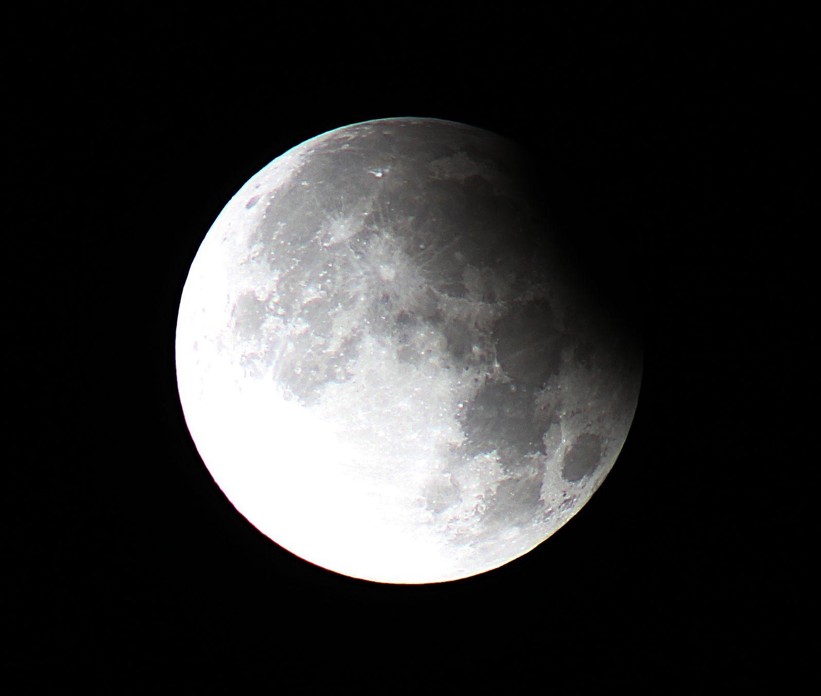 A bright Moon slight covered by Earth's shadow at upper right. On a dark background. 