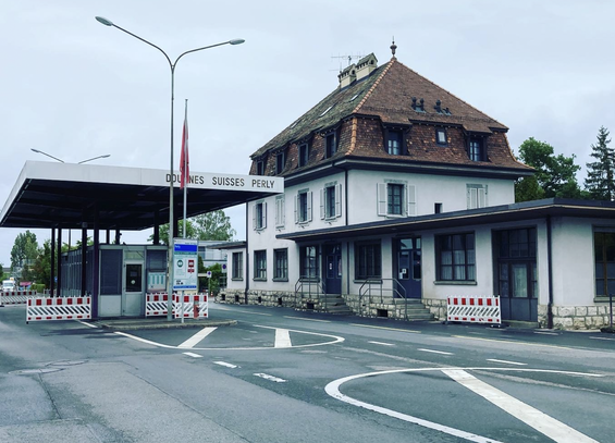 The photo of the place drawn in the previous image, starkly blueish-green in hue, showing the border post and a modern 1960s or 1970s roof over the road.