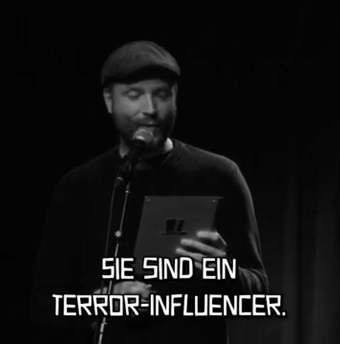 Marc-Uwe Kling hält ein Tablet vor sich und liest seinen Text. 

Untertitel: Sie sind ein Terror-Influencer.