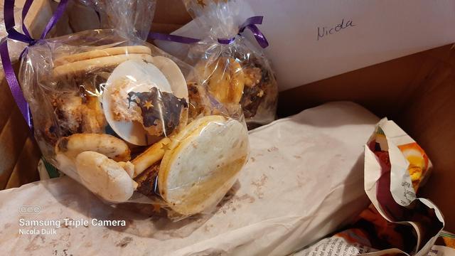 Ein Karton gefüllt mit frisch gebackenen Plätzchen, die in hübsche Weihnachtstüten verpackt wurden und ein Früchtebrot.