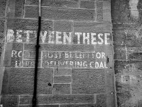 A stone wall with faded lettering reading "Between these...for delivering coal"