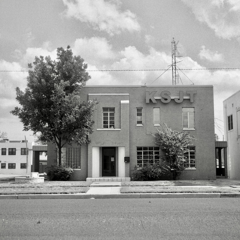 A black and white film photo. A vintage two-story brick building is home to radio station KSJT in San Angelo, Texas. Sunday, September 1, 2024.