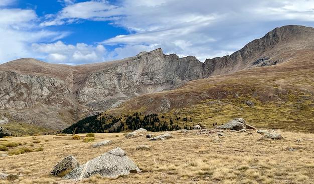 Photograph of mountains - above the tree line - blue sky and clouds in the background. 