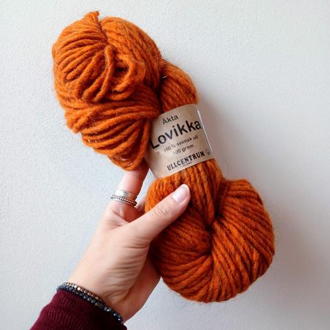 A skein of deep orange bulky weight yarn is held up against a white background.
