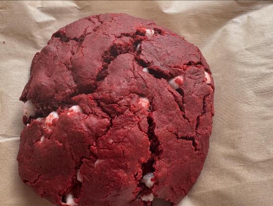Picture of a red velvet cookie lying on a paper napkin. The cookie has white chocolate chips in it which is something I don’t generally see in vegan food. 