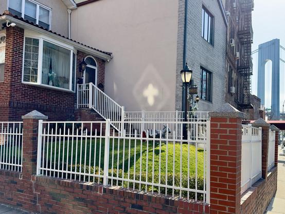 Two buildings in Bay Ridge, Brooklyn with the Verrazano Bridge in the background. The sun shining through a streetlamp makes a cross-shaped reflection on one of the building walls.