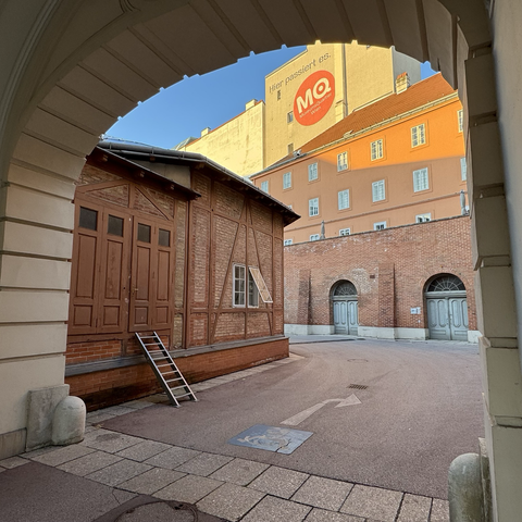The runner's view through an archway in the former imperial stables. Red bricks, a few wooden doors, blue sky, the early morning sun shining on the house facades.