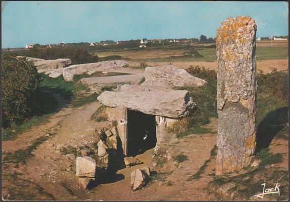 Printed semi-modern postcard showing the Pierres Plates dolmen at Locmariaquer in Morbihan, Brittany. An angled passage grave with several sculpted stones which lies at the end of the Locmariaquer peninsular overlooking Quiberon Bay. Part of the mound remains and the long chamber turns at about 45° part of the way down, and has a side chamber at the angle. From here another 10m of passage leads to the main chamber. A few scattered houses around Kerere can be seen in the distance. 