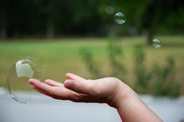 A bubble pops as it touches a fingertip. Some smaller, intact bubbles are also visible.