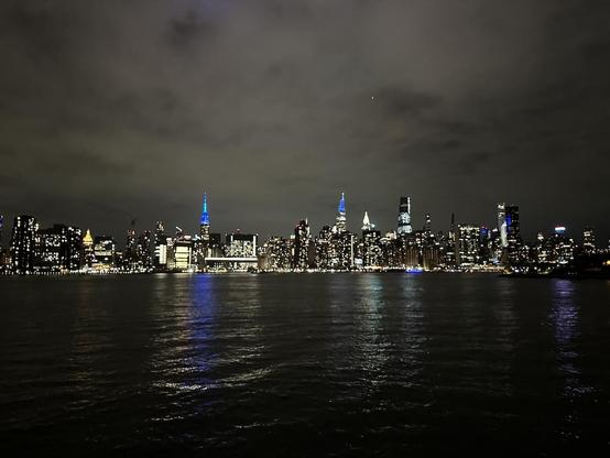 Night-time photo of the Manhattan Midtown skyline, seen from across the river. The spires of the Empire State Building and 1 Vanderbilt are both lit in blue, the ESB because the Giants won today and 1VB because that's its default color.