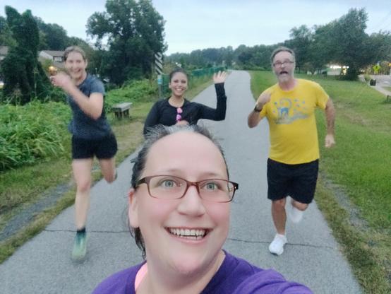 A selfie with four people. One person forward is taking the photo and people in the back are running. 