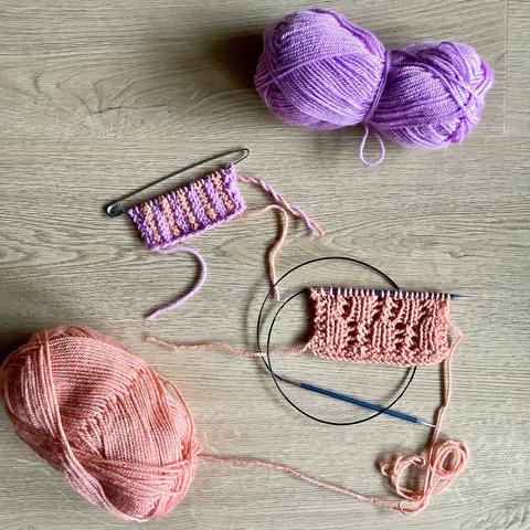 Knitted swatches in salmon pink and lilac yarn, shown together with their balls of yarn on a light wooden background.