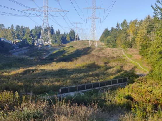 Shadows creep across a trail that runs under a power line, just carefully covering an old footbridge.