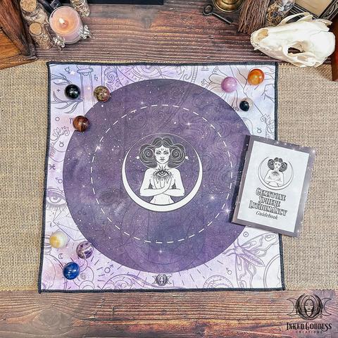 The contents of our Gemstone Sphere Lithomancy Set are arranged on a burlap-covered surface. It includes a square cloth in shades of purple with divination and third-eye imagery, nine different gemstone spheres, and a mini instruction booklet. This is an exclusive product from Inked Goddess Creations.